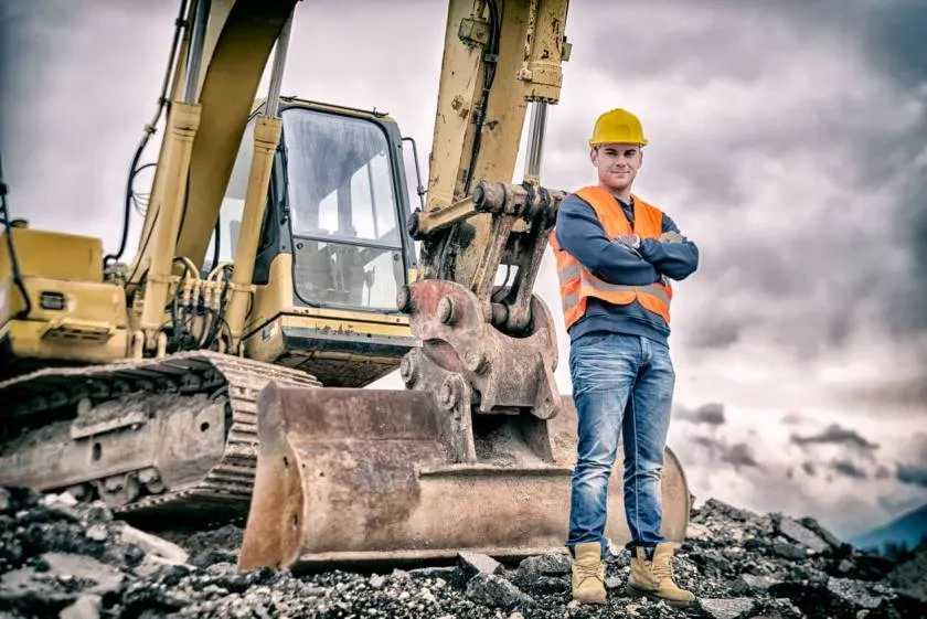 Heavy equipment operator standing beside an excavator on an active construction site